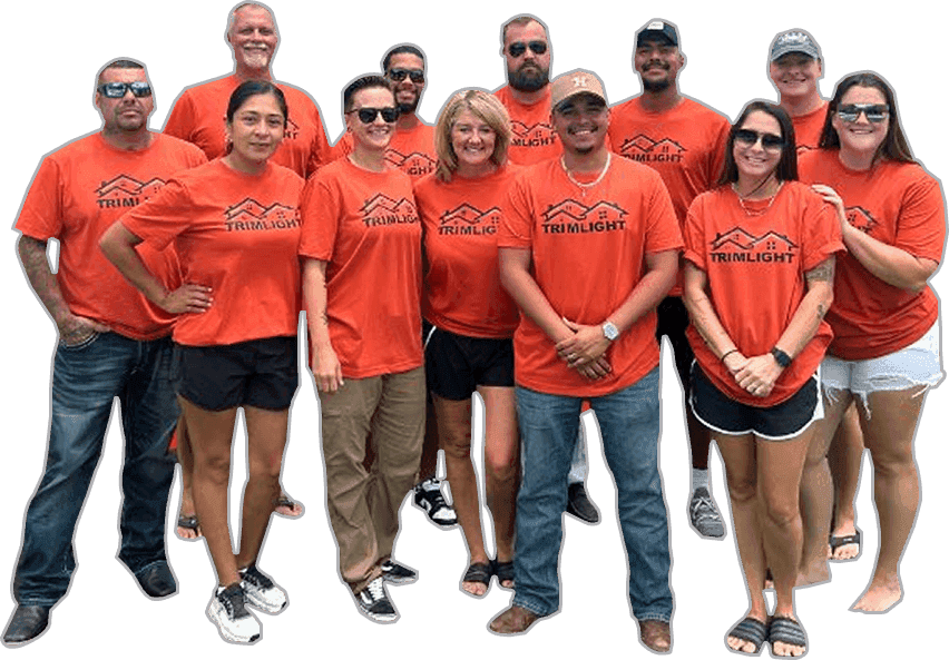 A group of twelve people stand together, smiling, all wearing matching orange Trimlight t-shirts. They are dressed casually, and some wear sunglasses. The background is white and plain. {{brizy_dc_image_alt imageSrc=