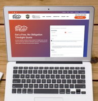 A laptop on a wooden table displays a quote request webpage. Beside it are a notebook with sketches, a pen, a smartphone, and a cup of coffee on a saucer. The scene suggests a workspace setting.